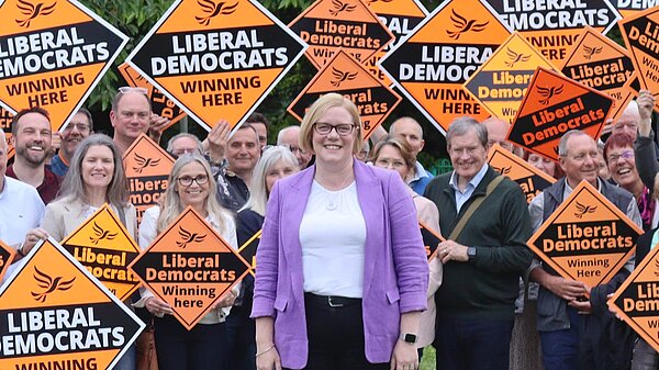 Zoe stands in front of a crowd of supporters, who are holding Lib Dem diamonds