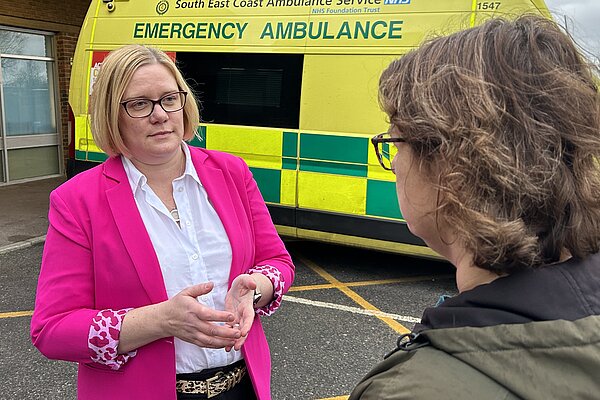 Zoe talks to a resident, they are both stood in front of an ambulance