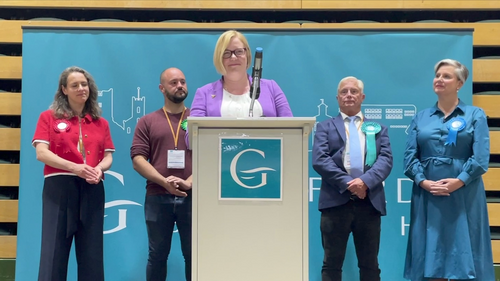 Zoe standing at a podium at the count, with the other candidates stood behind her