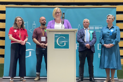 Zoe standing at a podium at the count, with the other candidates stood behind her
