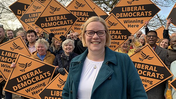 Zöe stands in front of a crowd of supporters, they are all holding large golden Liberal Democrat diamonds